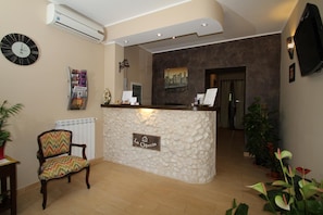 A reception area with a stone-textured counter, a clock, and a chair with a colorful cushion. - La Chioccia (Valmontone)