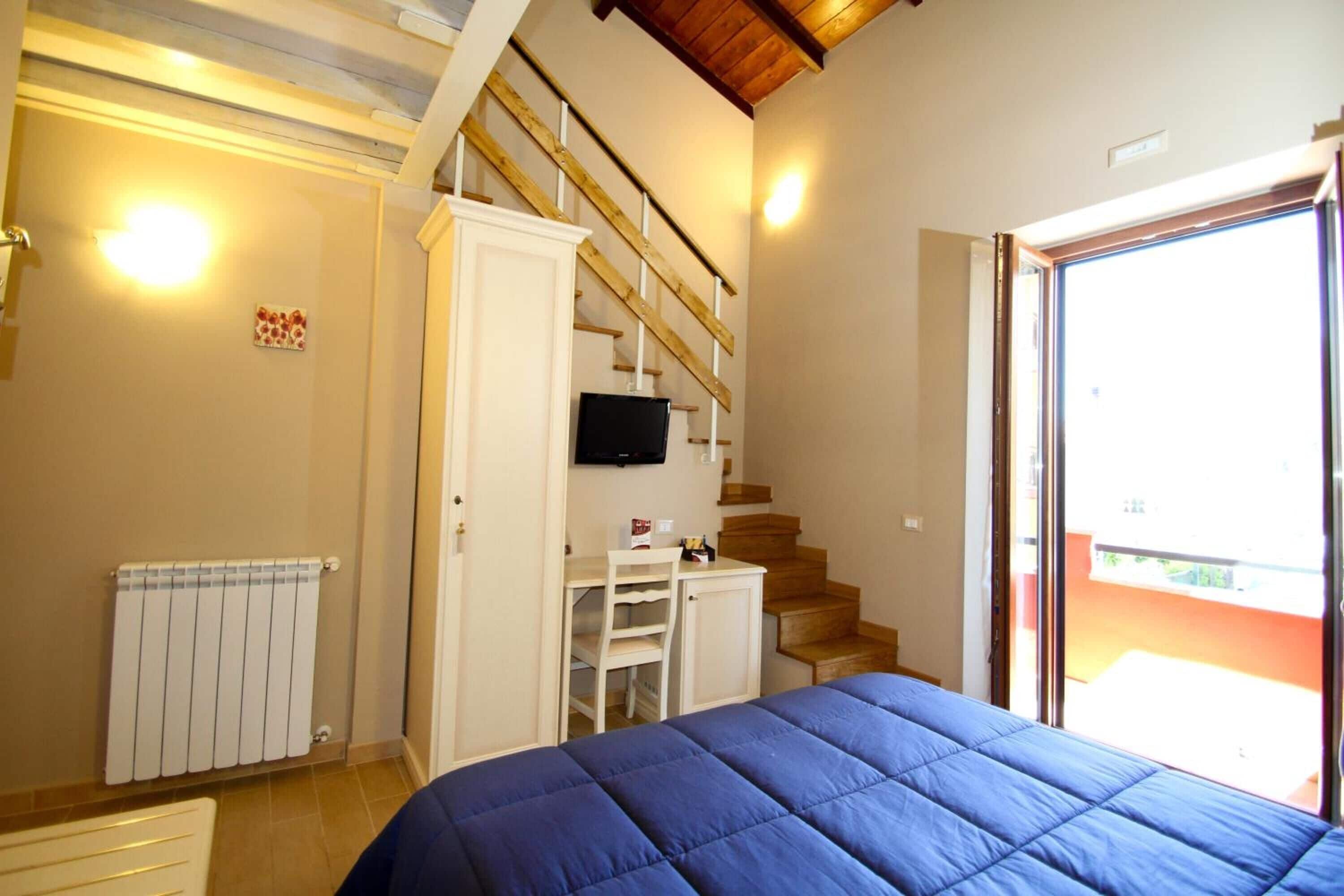 Un dormitorio con cama, televisor, armario, radiador y una escalera que lleva a un balcón.