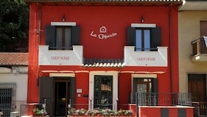 A red building with two 'GUEST HOUSE' signs, a red awning, and a small balcony. - La Chioccia (Valmontone)