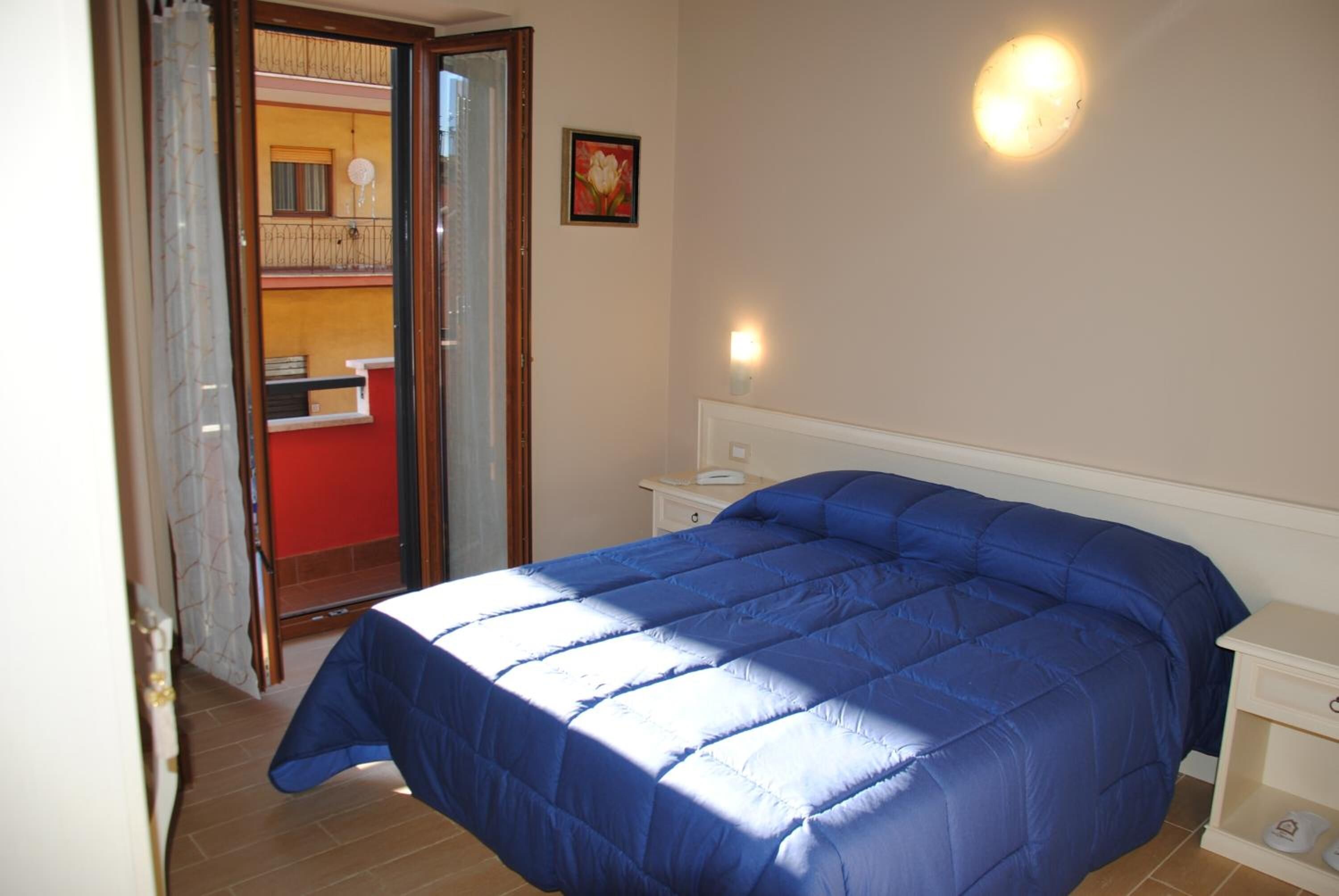 Una camera da letto con un letto grande, un comodino, una panca da notte e una porta che dà su un balcone.