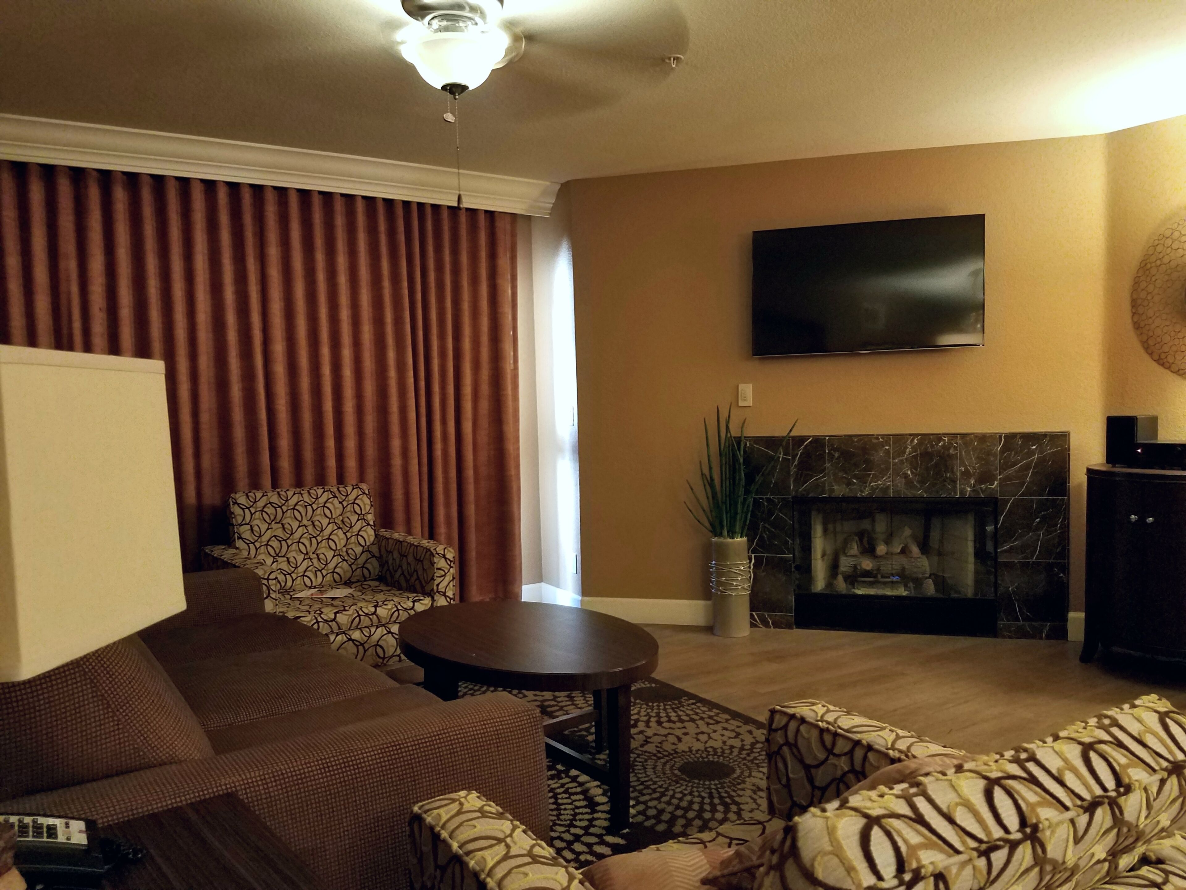 A living room with a sofa, armchairs, a coffee table, a flat-screen TV, a fireplace, and a ceiling fan.