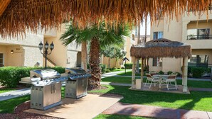 An outdoor patio area with a thatched roof, a grill station, and a gazebo.