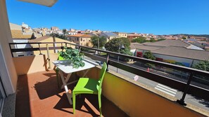 Un balcón con mesa y sillas, con vistas a una zona residencial con tejados de teja y un cielo azul despejado.
