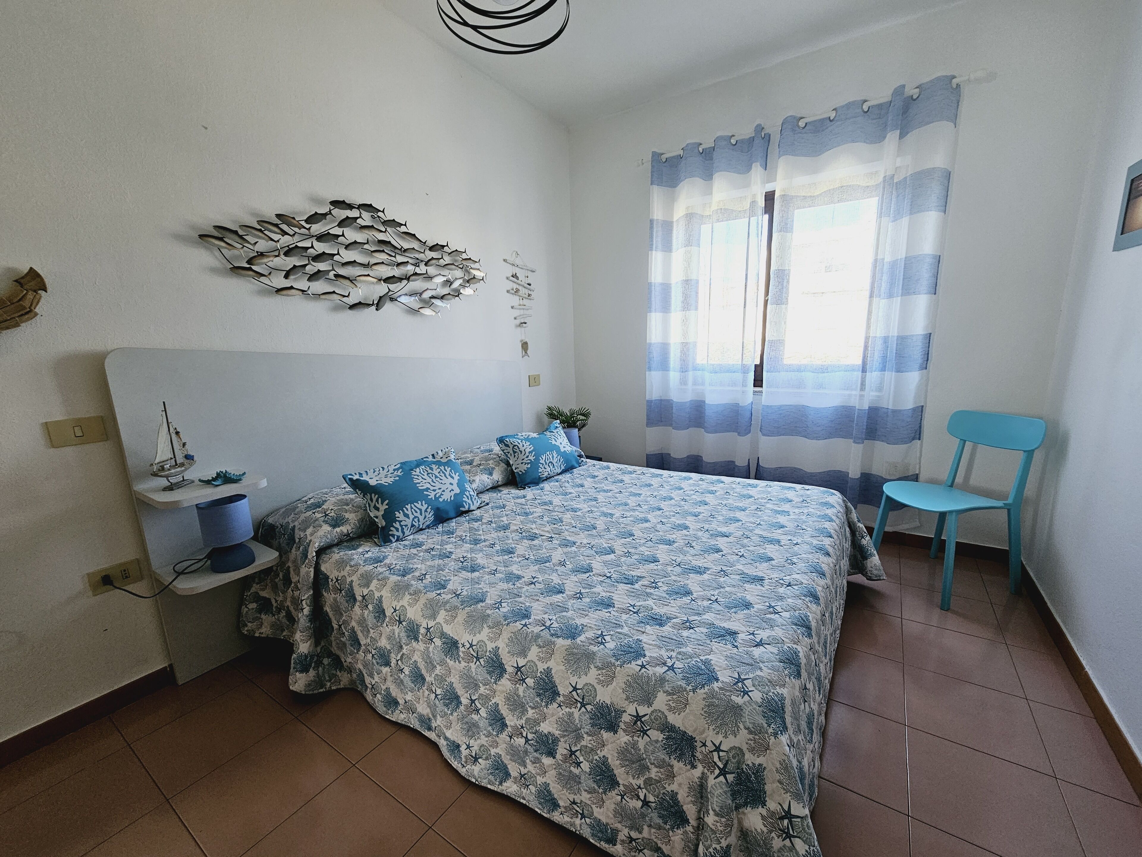 Ein Schlafzimmer mit einem Bett, einem Sessel, einem Regal mit einem Modellschiff und einer Wanddekoration.