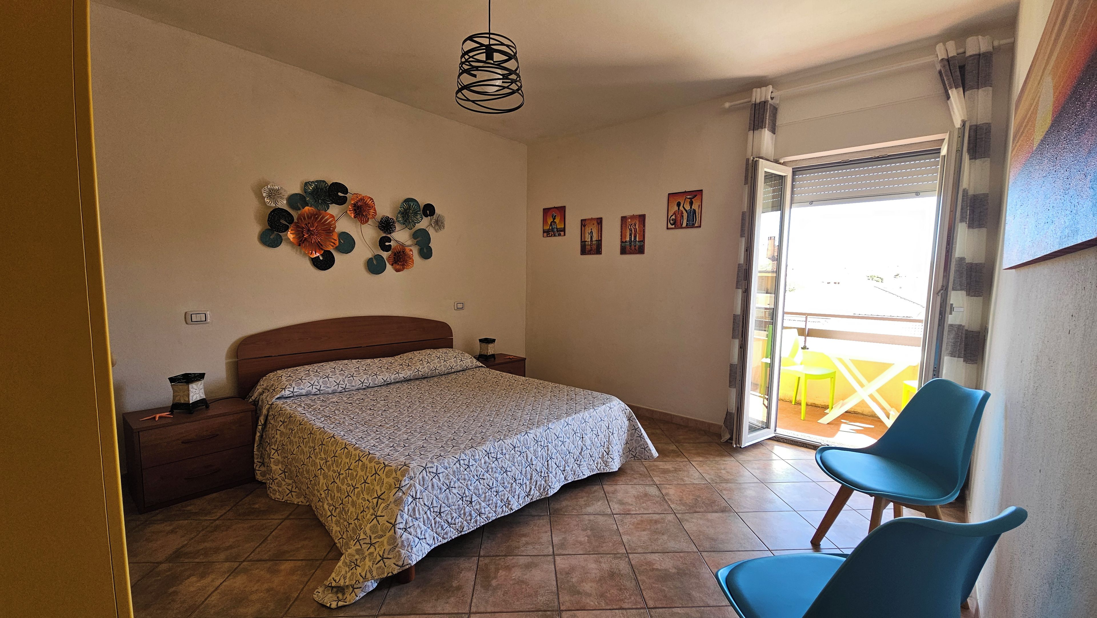 Ein Schlafzimmer mit einem Bett, einem Nachttisch, einem Wandbild und Blick ins Freie.