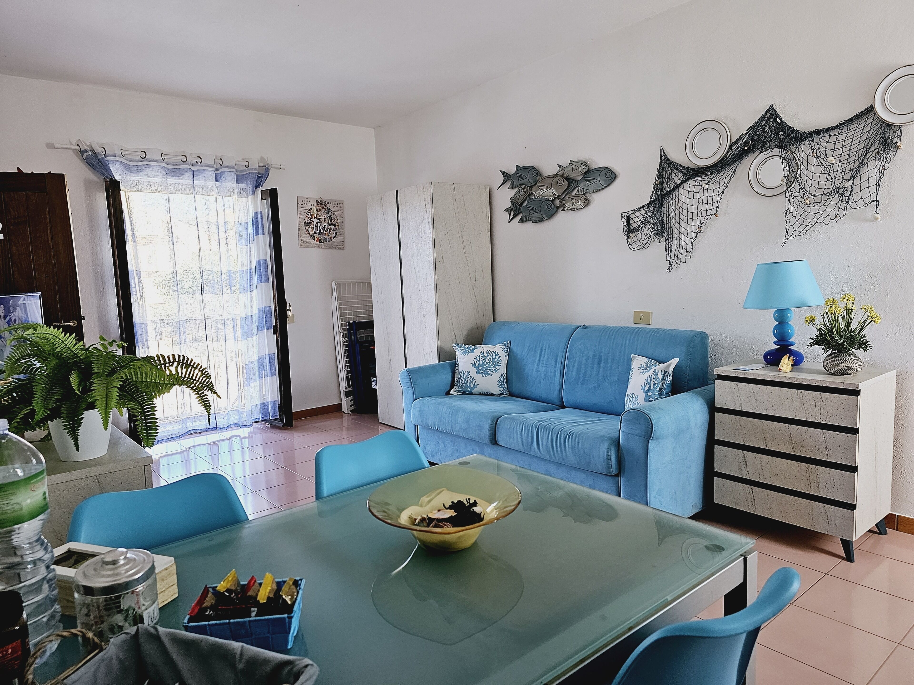 A living room with a blue sofa, a dining table with chairs, a blue lamp, and a decorative wall piece.