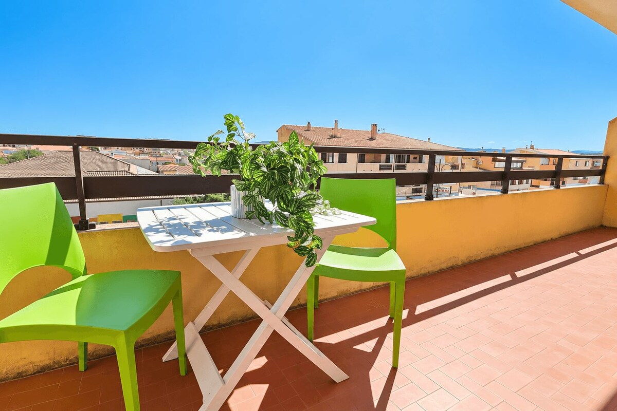 A balcony with a table and chairs, a potted plant, and a view of buildings in the background.