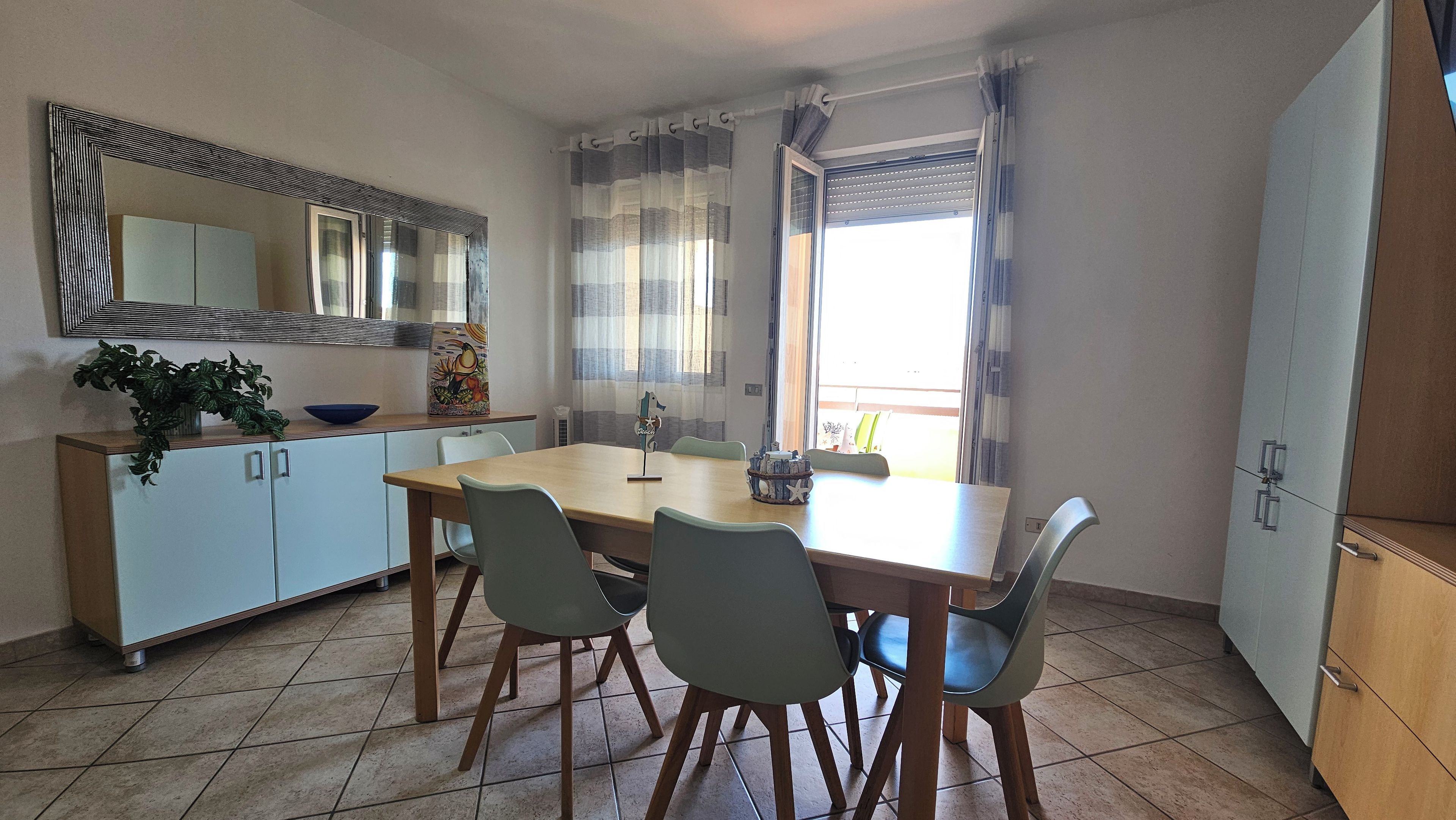 Uma sala de jantar com uma mesa de madeira, quatro cadeiras, um armário e um espelho.