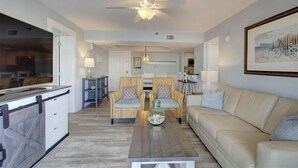 Ein Wohnzimmer mit einer Couch, zwei Sesseln, einem Couchtisch, einem Deckenventilator und einem Essbereich im Hintergrund.