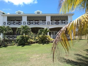 A two-story building with a balcony and a garden in front. - Mill House Guesthouse (Basseterre)