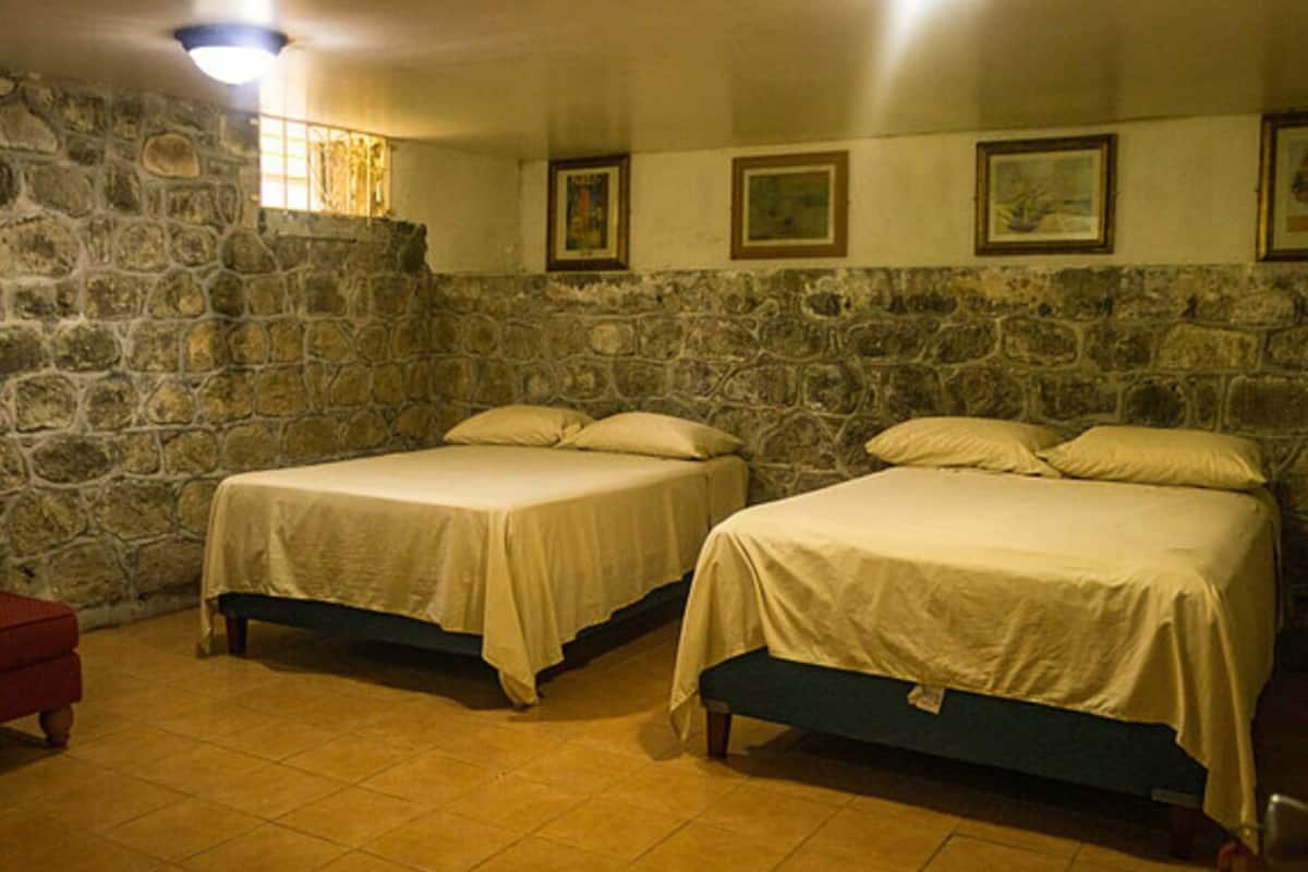 A room with two beds, stone walls, and a tiled floor.