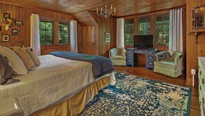 A cozy log cabin bedroom with a large bed, a desk, a television, and a chair.