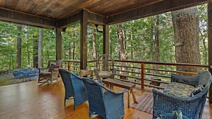 An outdoor deck with wicker furniture, wooden flooring, and a view of a forest.