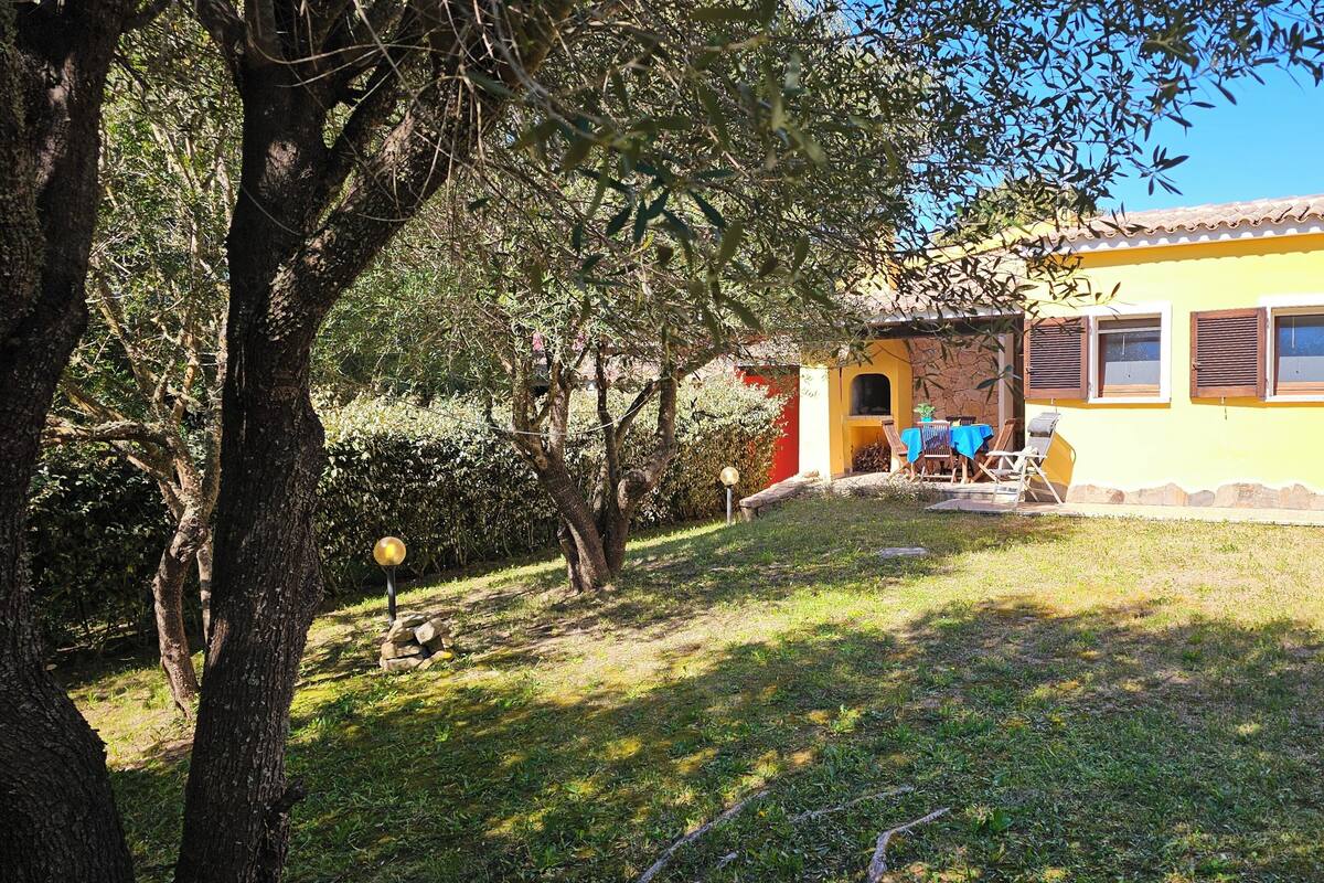 Un edificio amarillo con pared de piedra, un patio con sillas y un árbol en primer plano.
