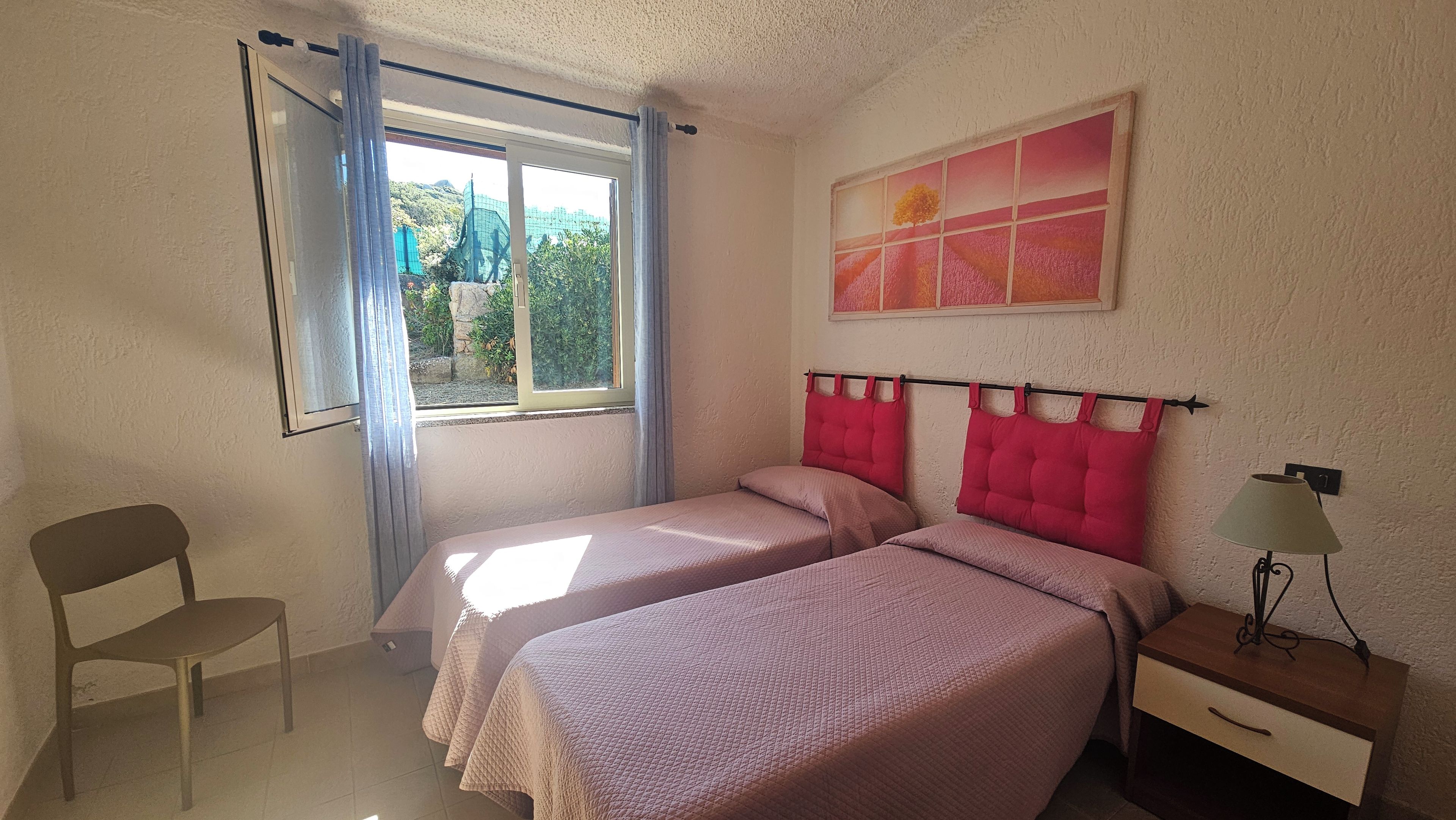 Une chambre avec deux lits, une chaise, une table de chevet et une fenêtre avec des rideaux.