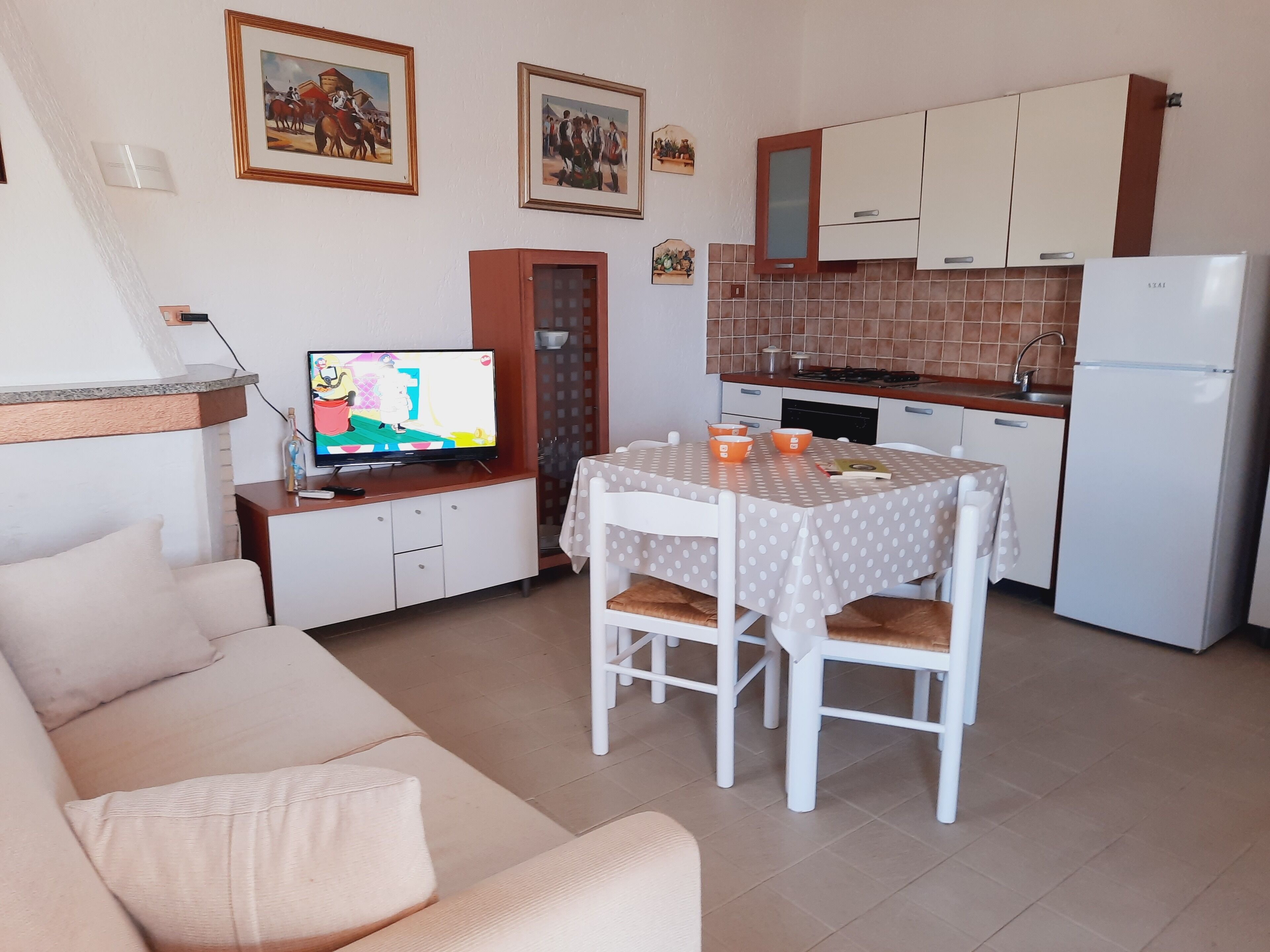 Un ambiente compatto con angolo cottura, zona pranzo con tavolo e sedie, divano e televisione.