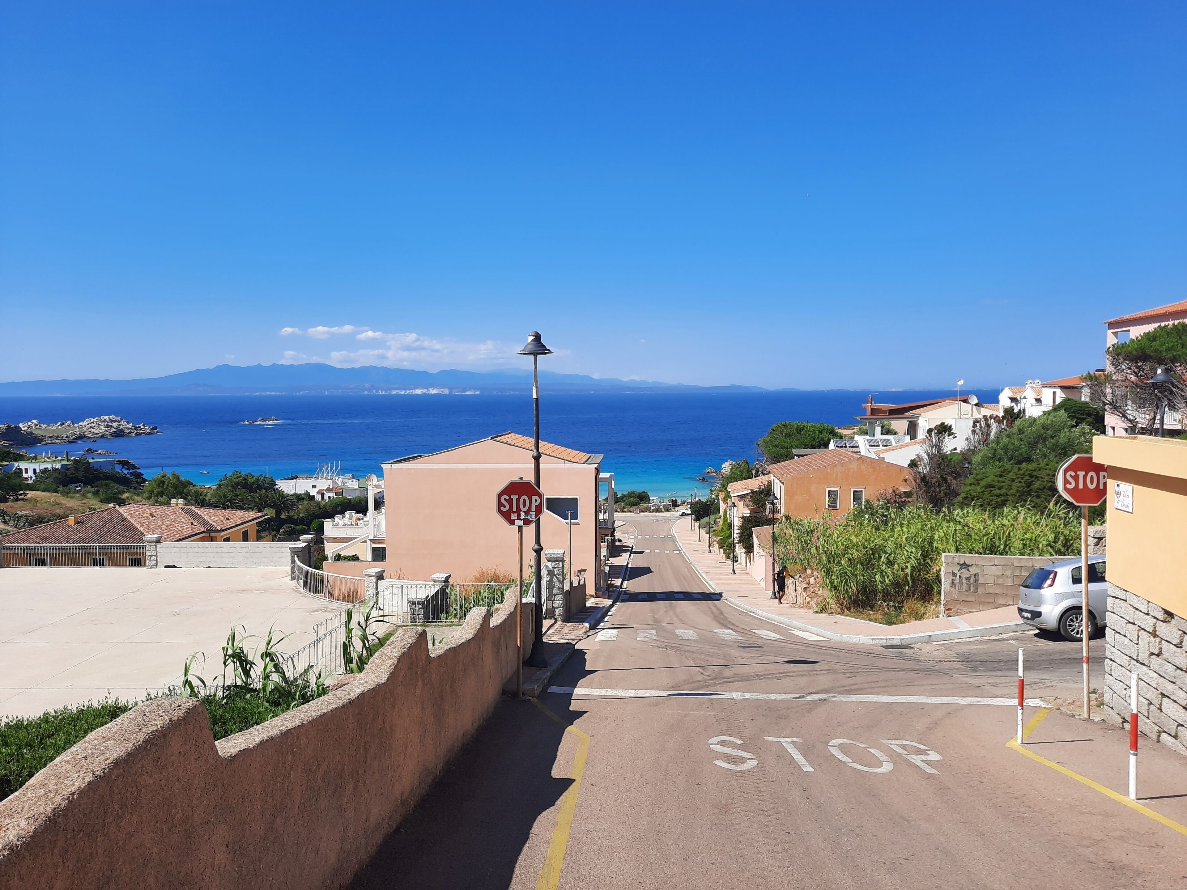 A coastal street with a stop sign, a clear view of the sea, and buildings with Mediterranean architecture.