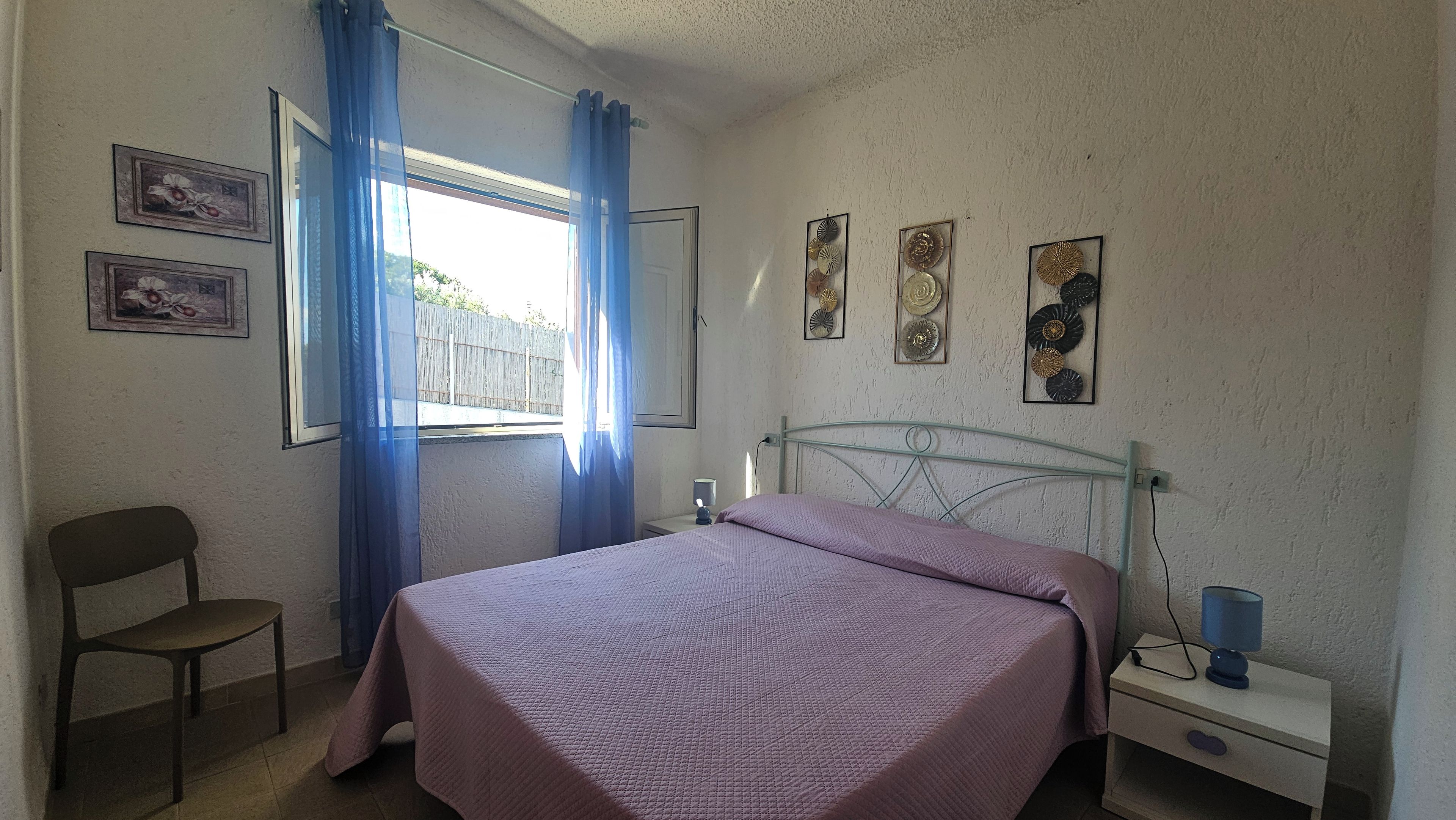 Une chambre à coucher avec un lit, une chaise, une table de chevet avec une lampe et une fenêtre avec des rideaux.