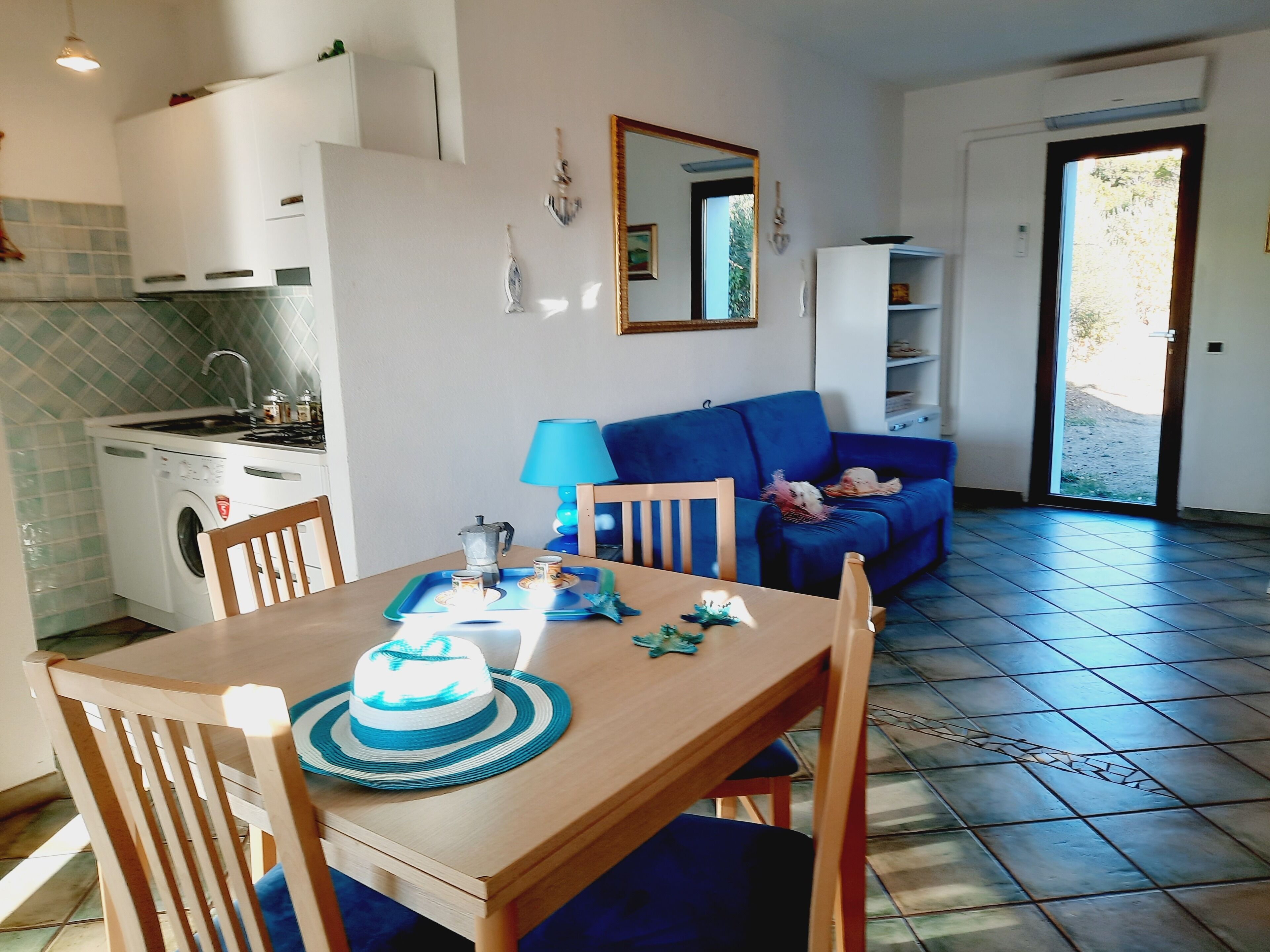 A compact living space with a dining table, chairs, a sofa, a kitchen area, and a door leading outside.