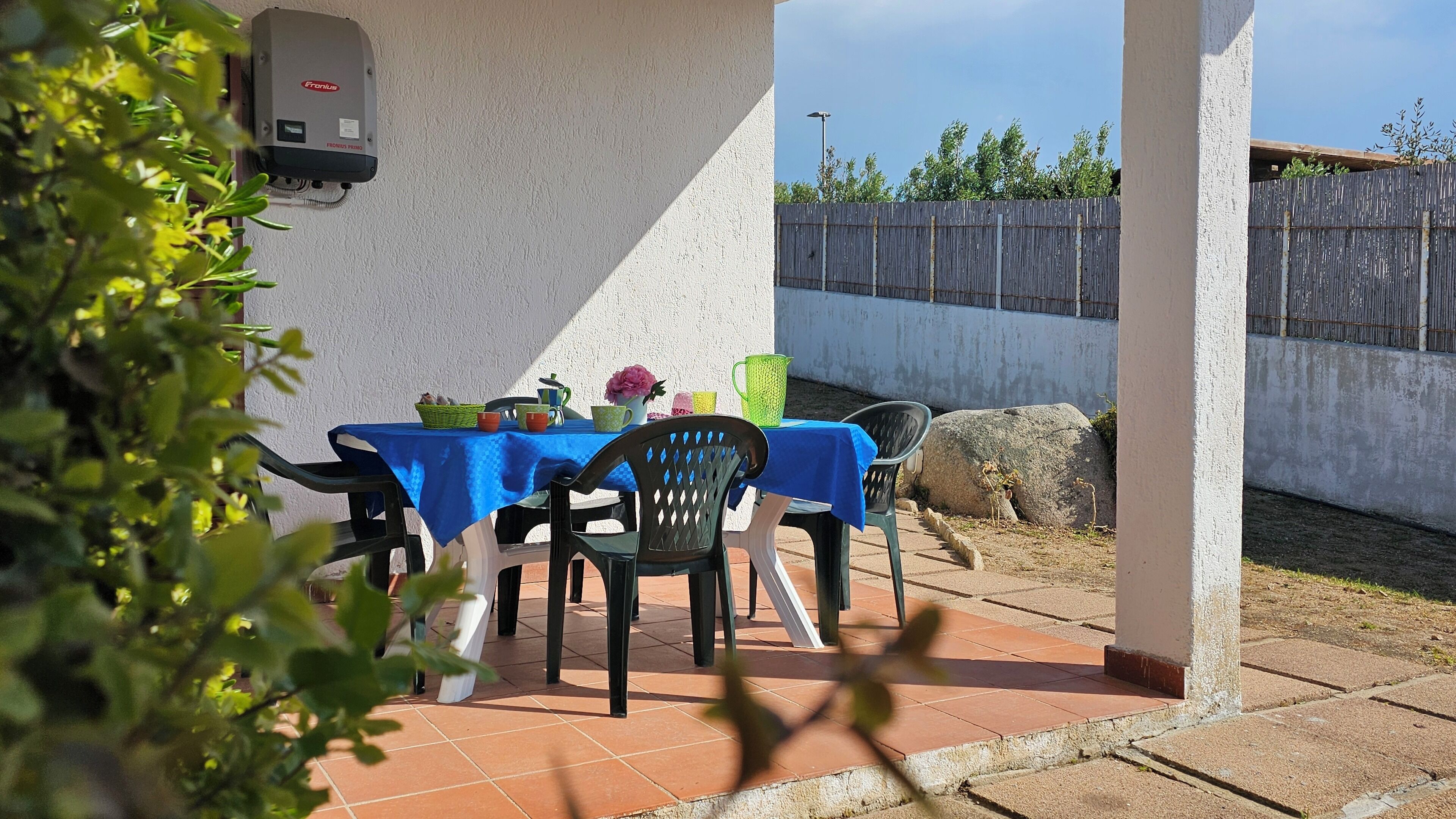 Une terrasse extérieure avec une table dressée pour deux personnes, recouverte d’une nappe bleue et entourée de chaises.