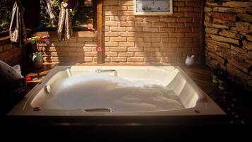 Un bain à remous dans une pièce rustique avec un mur en briques, un plancher en bois et une petite fenêtre.
