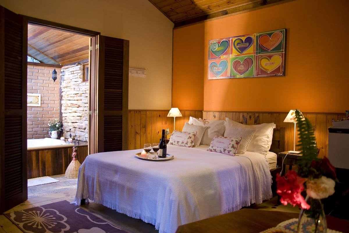 Um quarto aconchegante com parede de pedra, teto de madeira e uma cama com colcha branca.