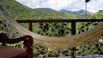 A hammock on a wooden deck with a view of lush green mountains.