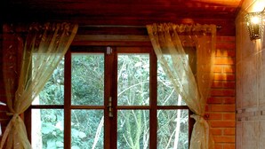 Una cabaña de madera con un ventanal grande, una bañera con velas y pétalos de rosa.