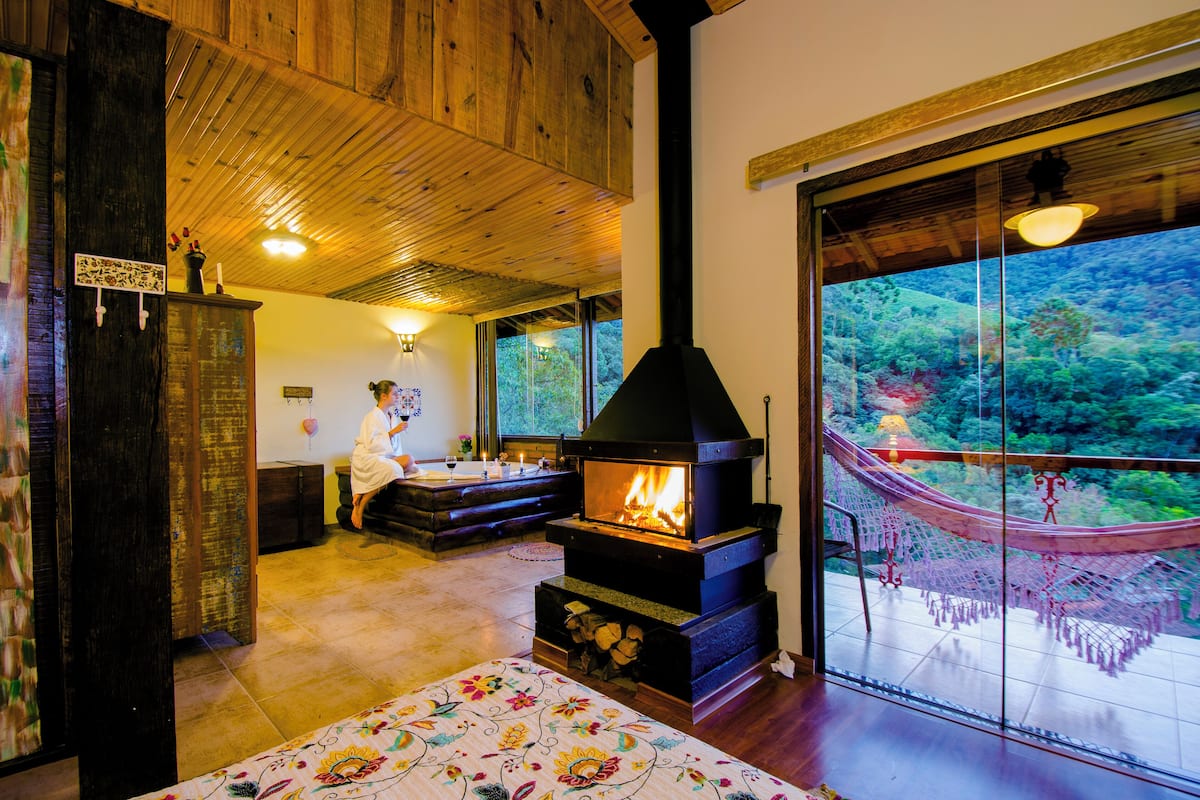 Um quarto aconchegante com lareira, área de refeições e uma grande janela com vista para o verde.