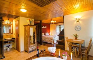 Quarto aconchegante com teto de madeira, uma cama com roupa de cama florida, uma mesa de madeira com um vaso e um relógio de parede.