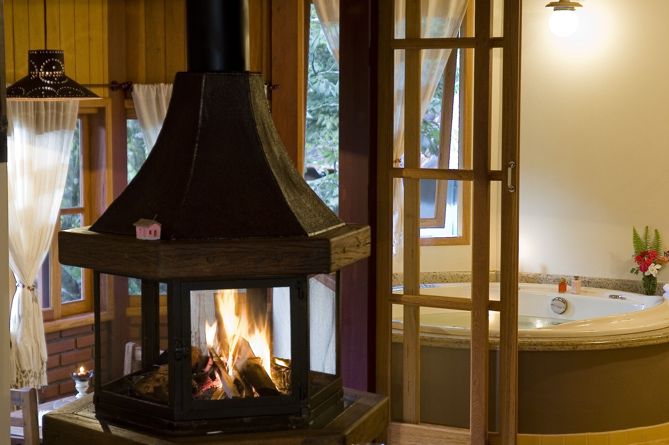 A wood-burning stove with a chimney, a bathtub, and a window with curtains.