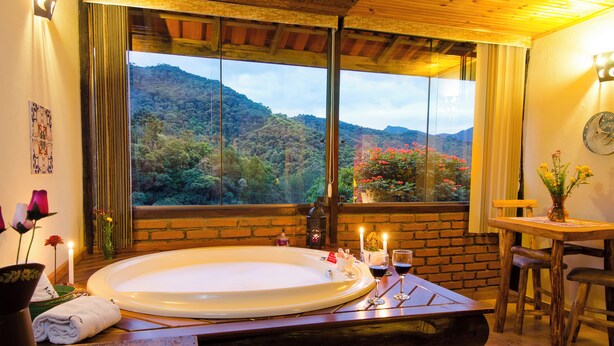 Un baño con una bañera grande, una mesa de madera y vistas a una ladera boscosa.