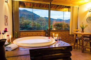 Un baño con una bañera grande, una mesa de madera y vistas a una ladera boscosa.
