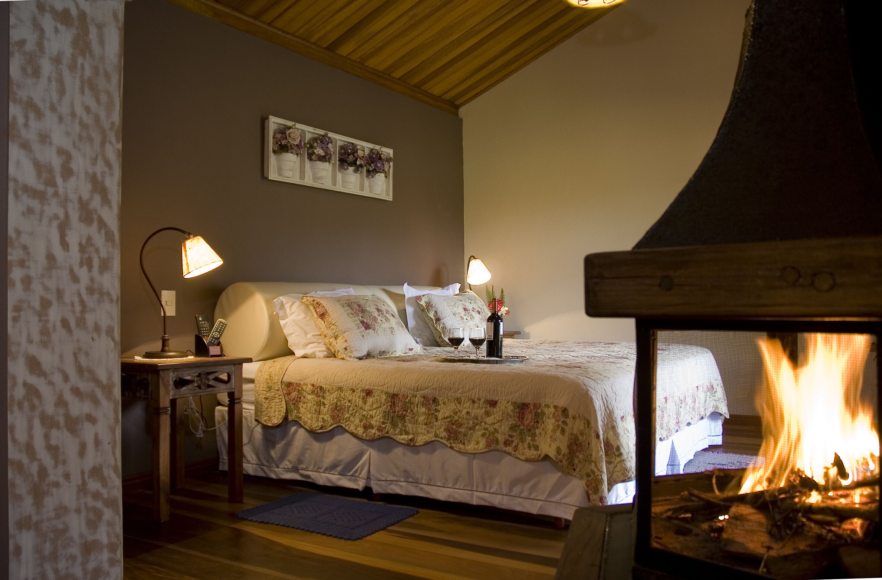 A cozy bedroom with a bed, two bedside lamps, a fireplace, and a wall-mounted picture.