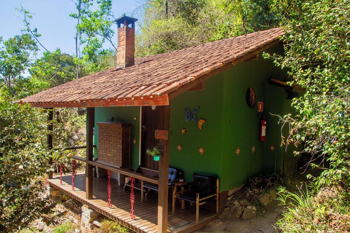 Uma cabana rústica com deck de madeira, chaminé de tijolos e exterior verde.