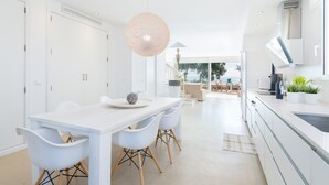 A modern kitchen with white cabinetry, a dining area with white chairs, and a large pendant light. - PORT NOU CA NA CATI - Chalet with sea views in Cala Bona. Free WiFi (Son Servera)