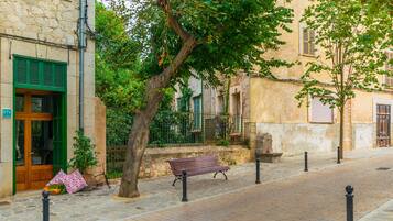 A cobblestone street with a bench, a tree, and a building with a stone facade and green shutters.