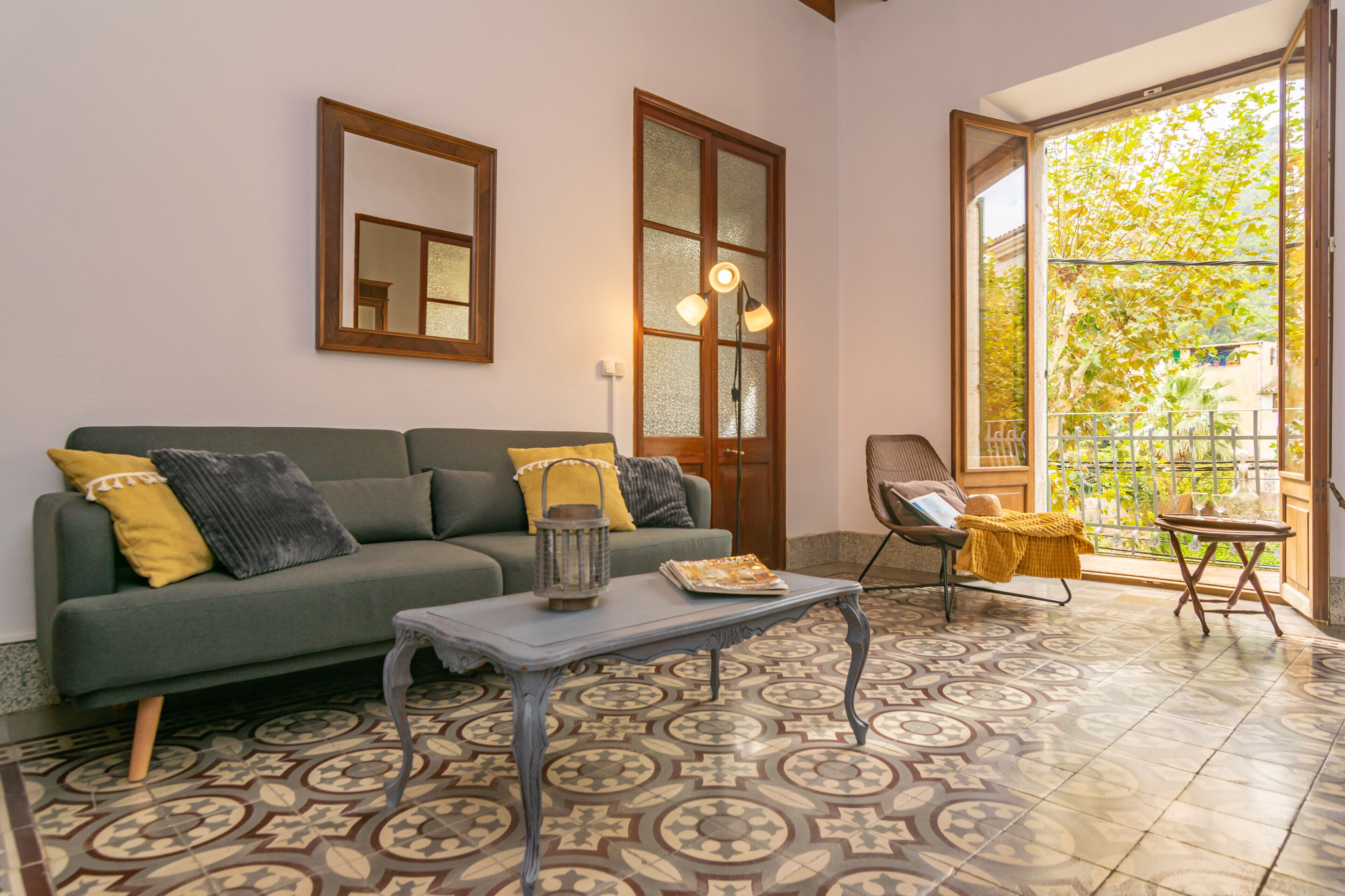 Una sala de estar con sofá verde, baldosas de suelo con diseño, una mesita y un balcón con vistas a zonas verdes.