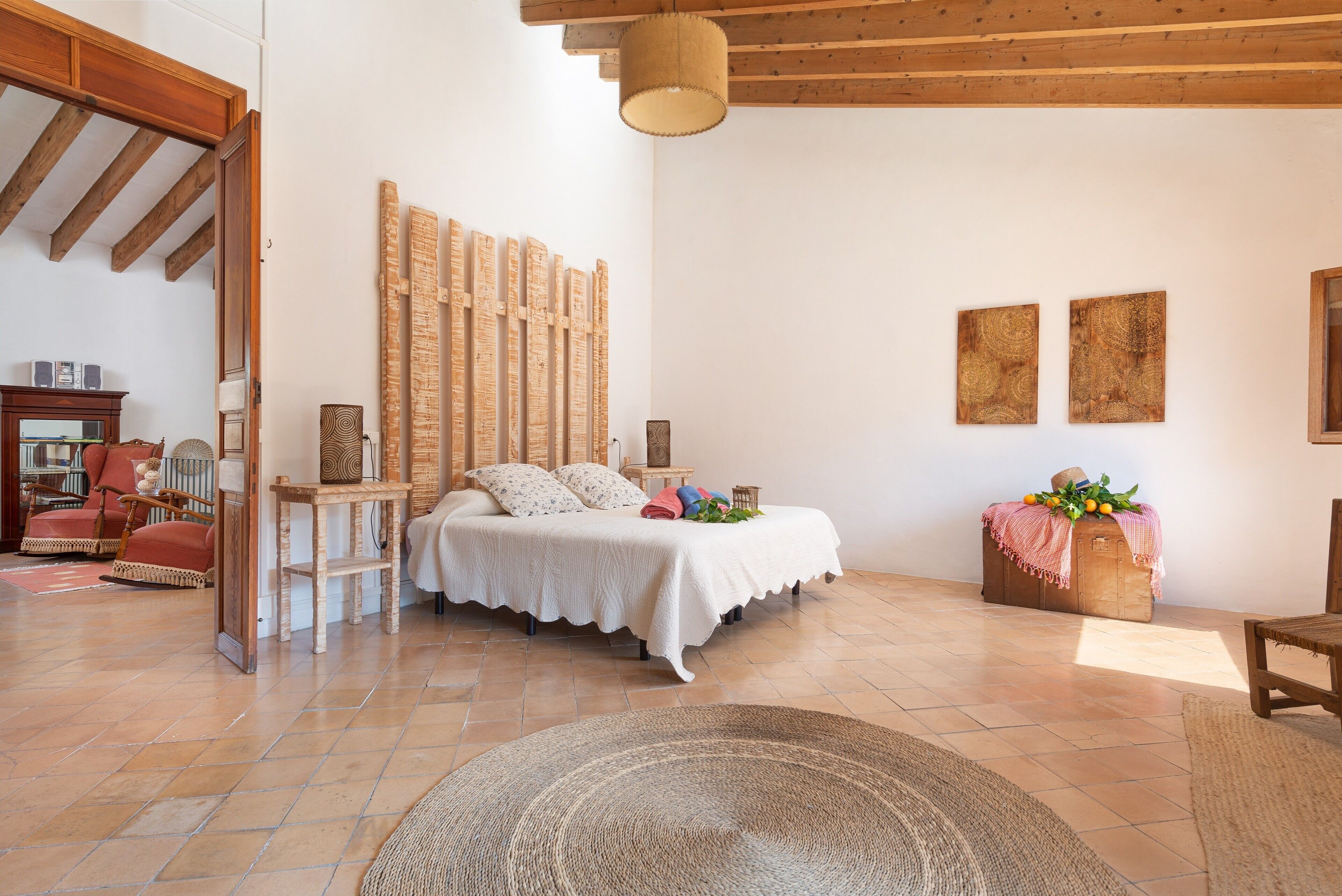 Un dormitorio con cama, cabecero de madera, dos cuadros en la pared, un aparador de madera y una mecedora.