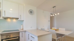 Een moderne keuken met witte kasten, een inbouwoven en een eethoek met een witte tafel en stoelen.