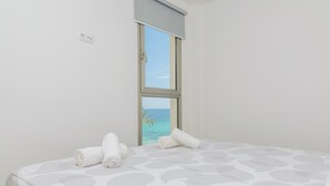 Een slaapkamer met een bed, een raam met uitzicht op zee en een stopcontact aan de muur.