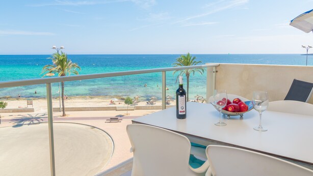 Een balkon met een tafel, een fles wijn en een schaal fruit.