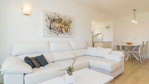 Een moderne woonkamer met een witte modulaire bank, een salontafel met een plant, en een eethoek met een tafel en stoelen.