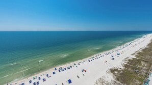A beach with a long stretch of white sand, clear blue water, and numerous umbrellas.