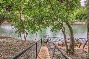 A wooden staircase leading to a viewing platform with a metal railing, overlooking a calm river with trees in the background.