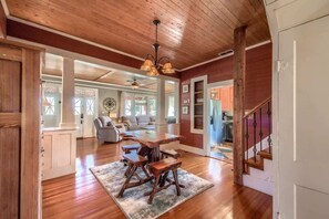 A spacious living area with a wooden ceiling, a dining table with chairs, a sofa, and a staircase.