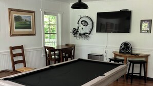 Ein Billardtisch in einem Raum mit weißen Wänden, ein darüber montierter Fernseher und eine Dekoration mit einem gerahmten American-Football-Helm.