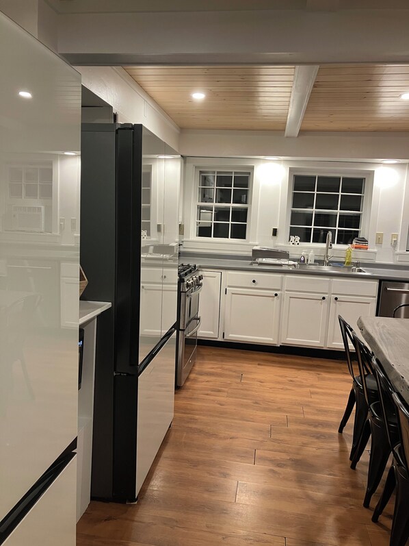 A modern kitchen with white cabinets, a stainless steel refrigerator, and a wooden floor.