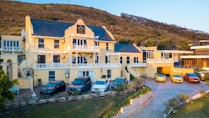 A multi-story hotel with a balcony, parking area, and a hilly backdrop. - Cape Grandeur (Cape Town)
