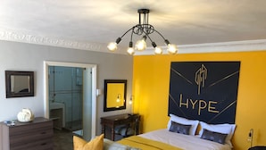 A hotel room with a bed, a sofa, a dresser, a mirror, and a bathroom visible through an open door. - Cape Grandeur (Cape Town)